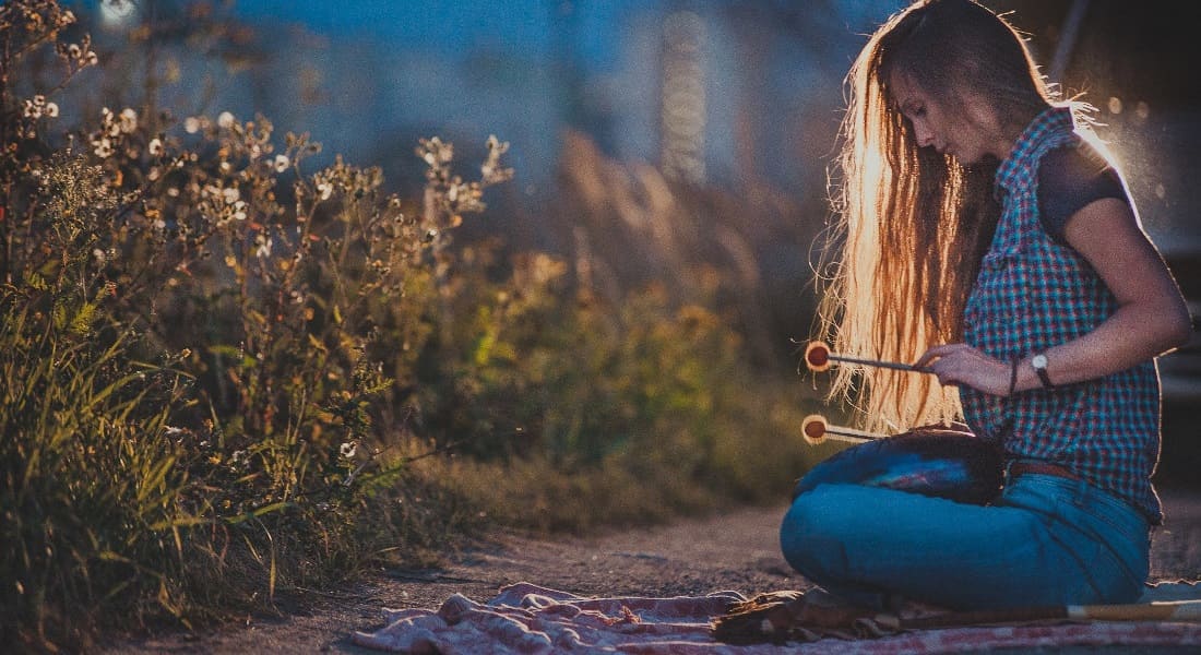 A woman sitting on the ground at night playing a tongue drum