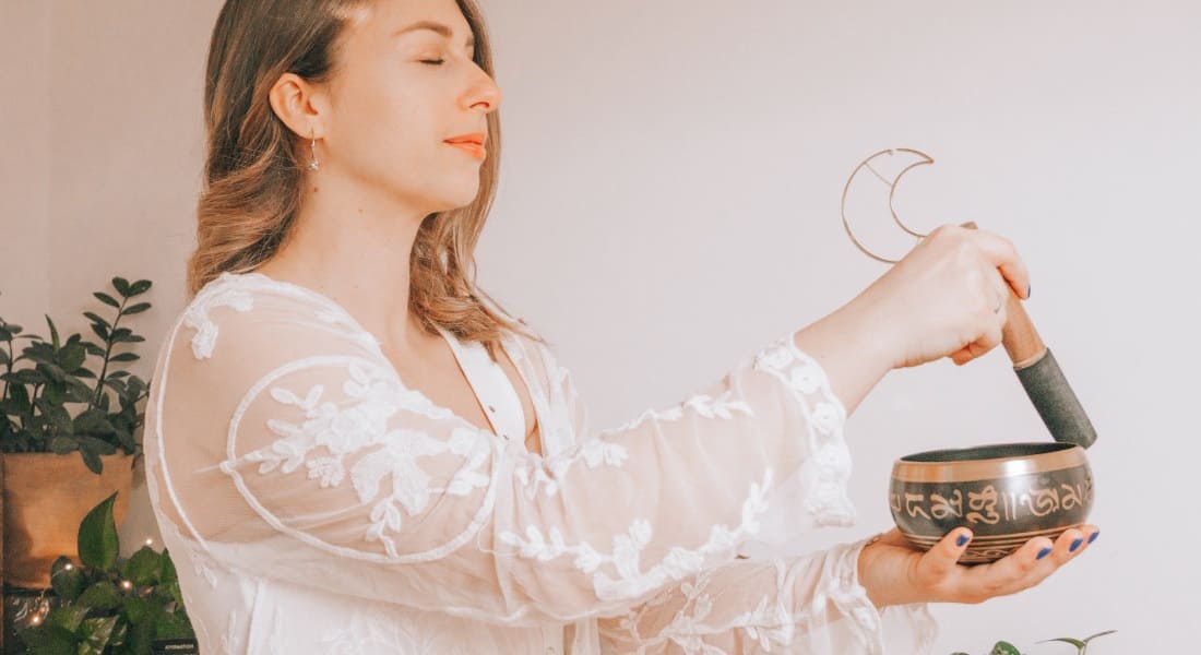 A woman standing with her eyes closed with a singing bowl
