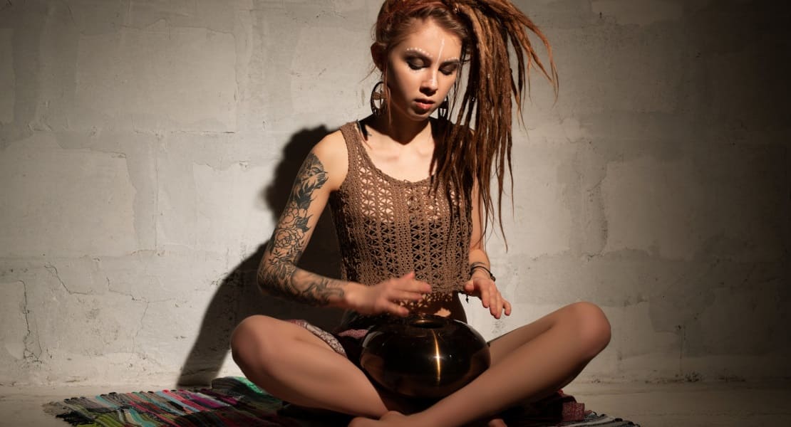 A woman with dreadlocks playing a tongue drum