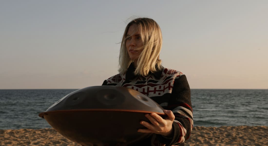 A woman with a handpan on a sandy beach