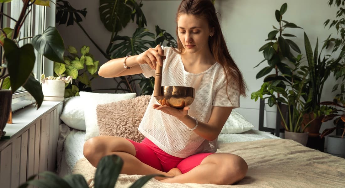 A young woman meditating on her bed with a singing bowl