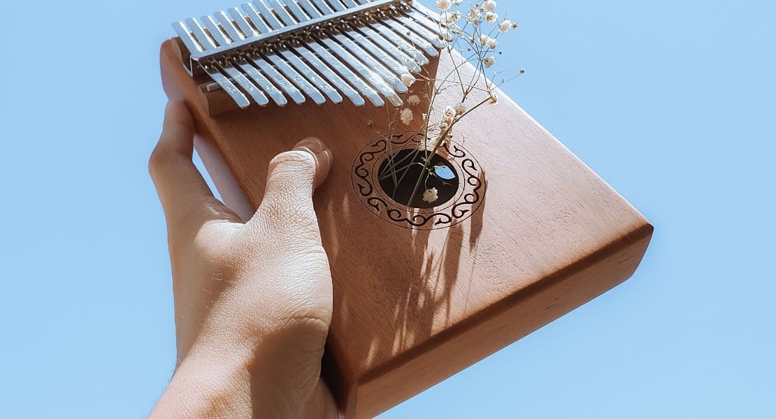 A wooden kalimba held up in the air with one hand