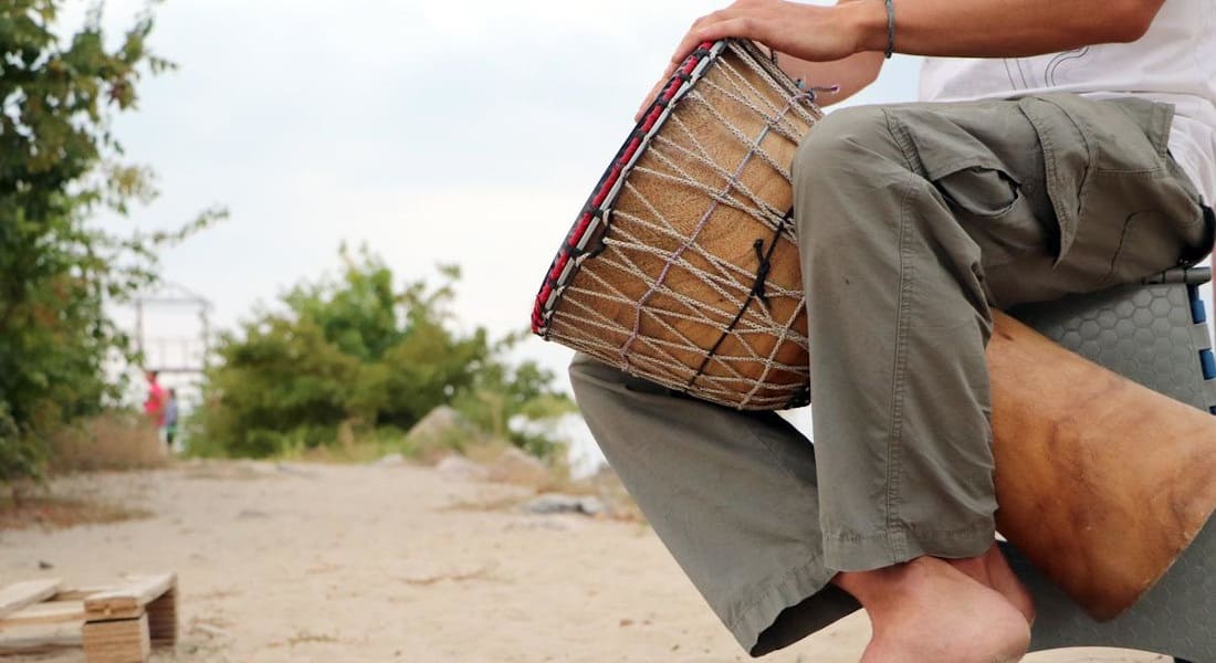 A man on the beach playing a large djembe