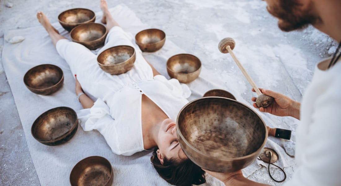 A man performing a sound massage with several Tibetan bowls on a woman lying down