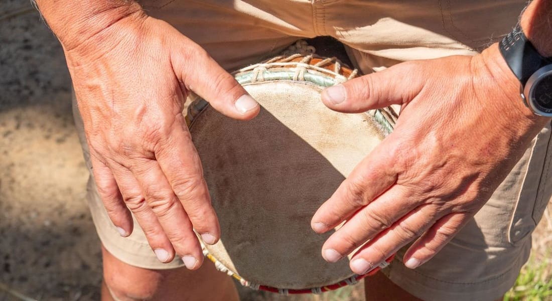 A man playing a small djembe between his legs