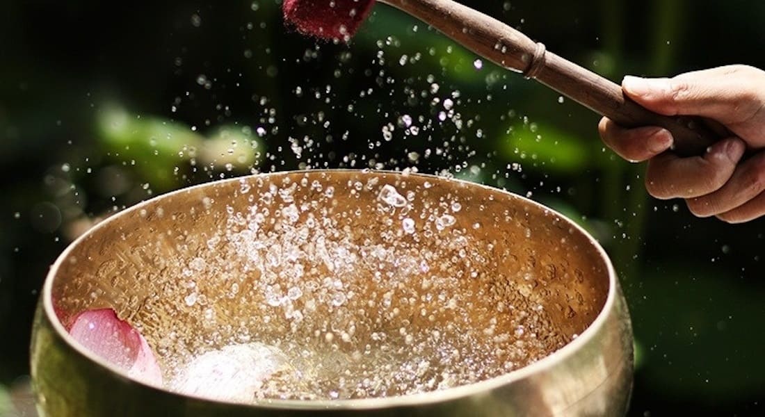 A metal Tibetan singing bowl filled with water struck with a mallet