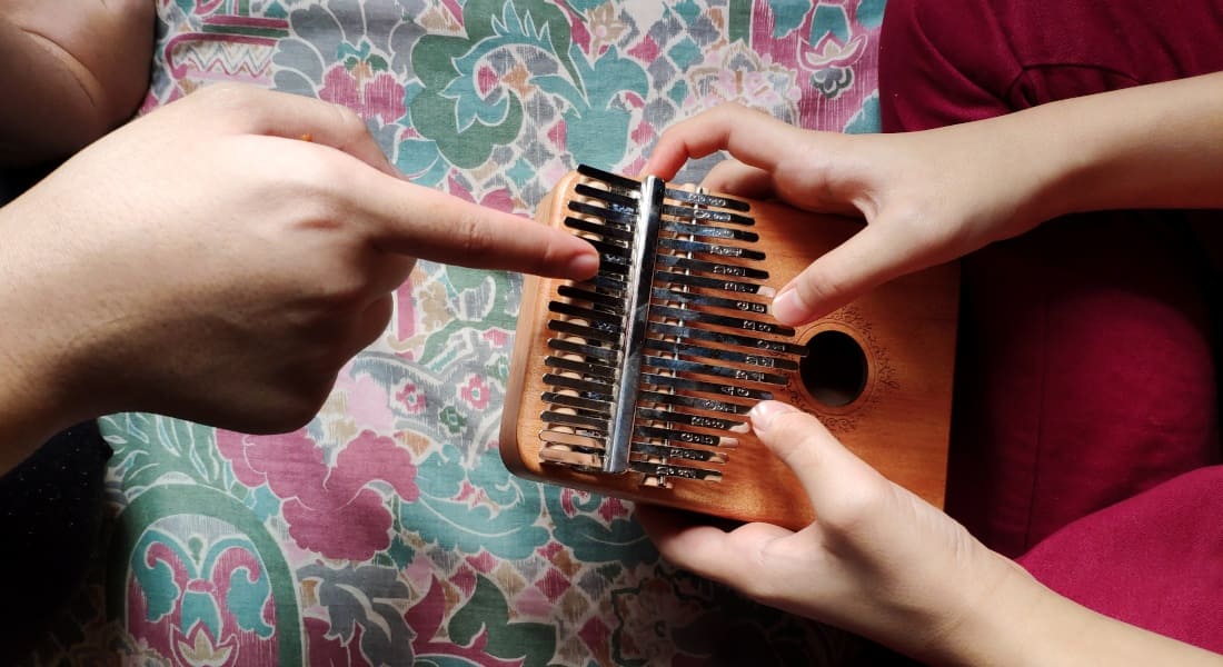 A person holding a kalimba while another helps them play