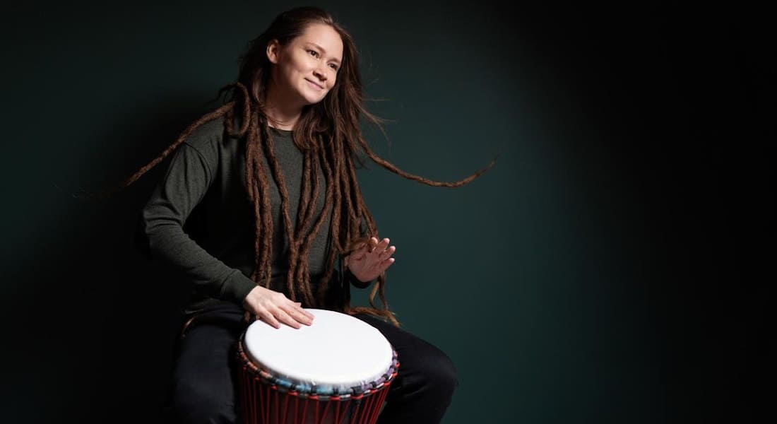 A white woman playing the djembe