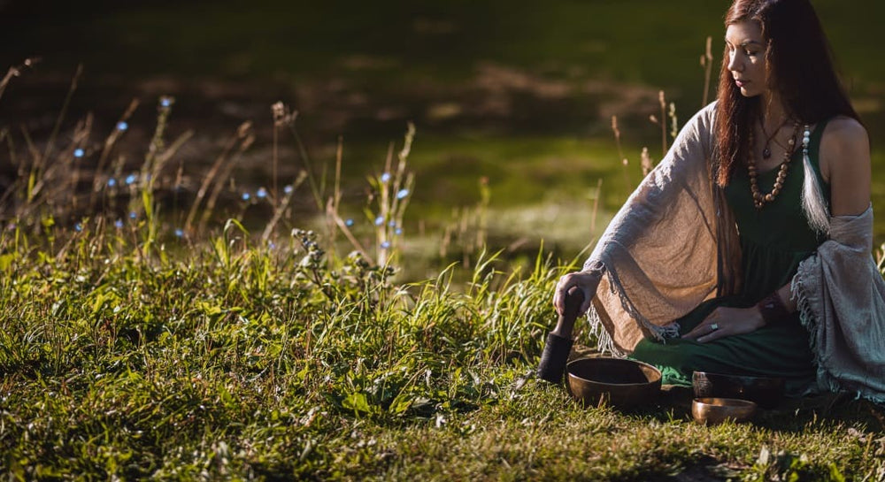 A woman sitting in the grass meditating with a singing bowl