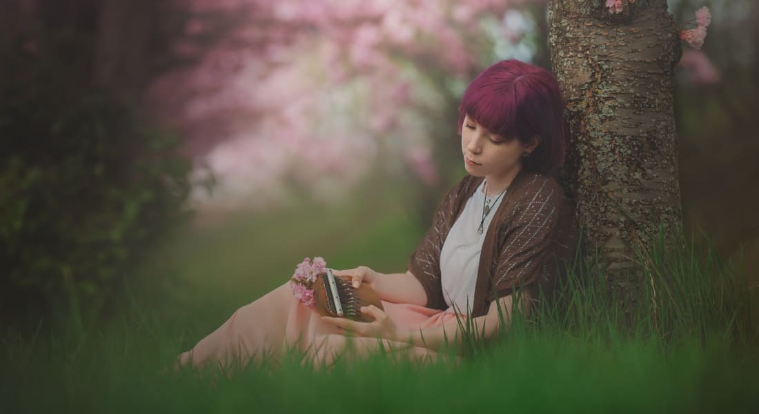 A woman sitting in the grass playing a thumb piano