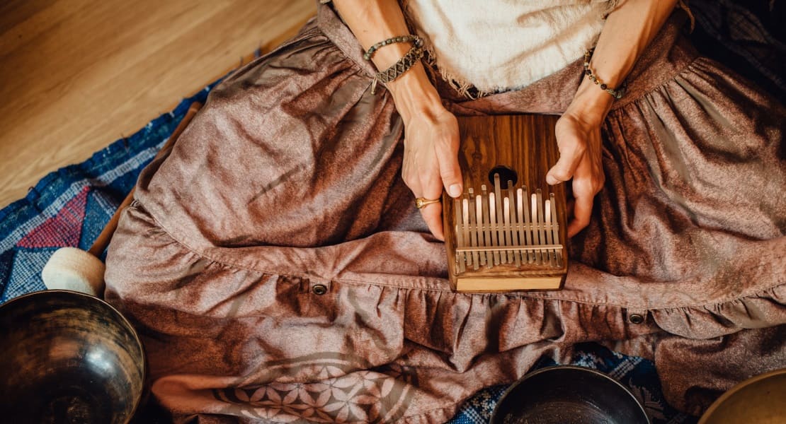 A woman sitting on the floor cross-legged playing kalimba