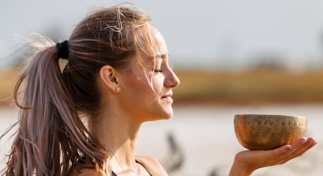 A woman with her eyes closed holding a Tibetan singing bowl in one hand