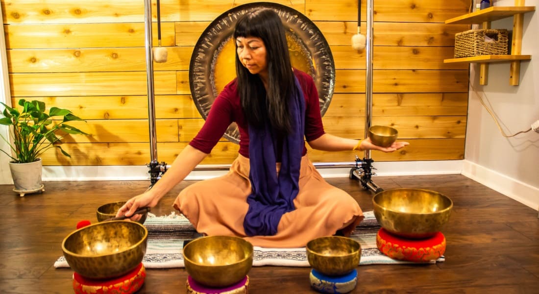 An Asian woman giving a sound bath with Tibetan singing bowls