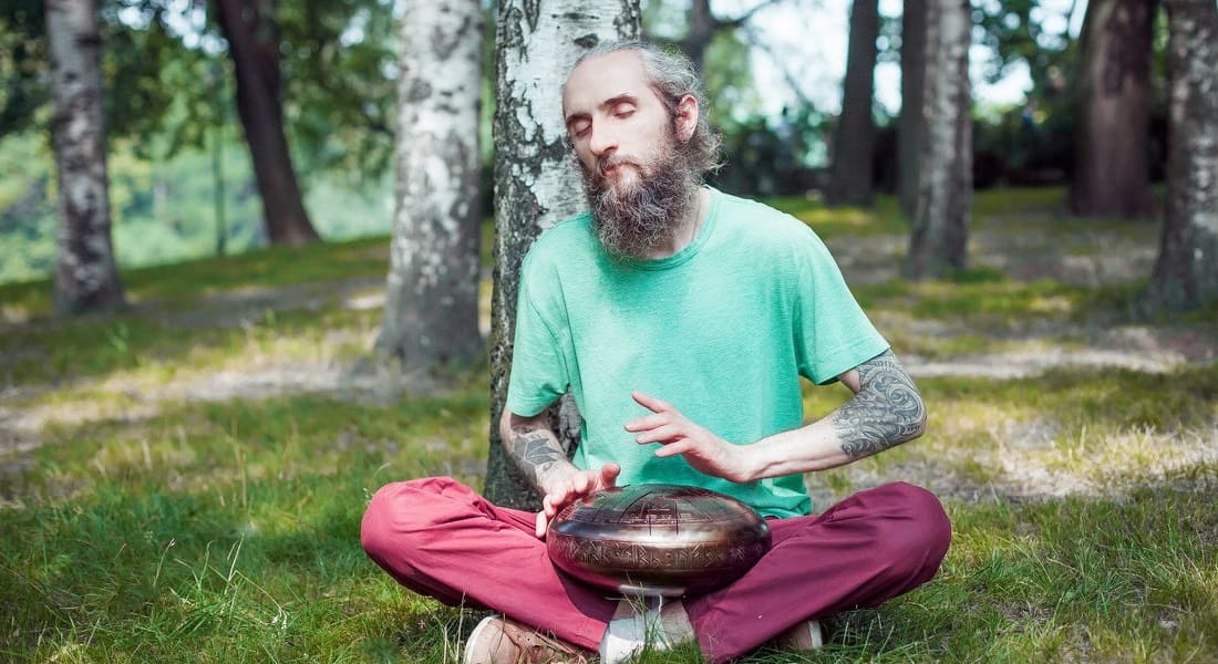 A bearded man meditating with a tongue drum