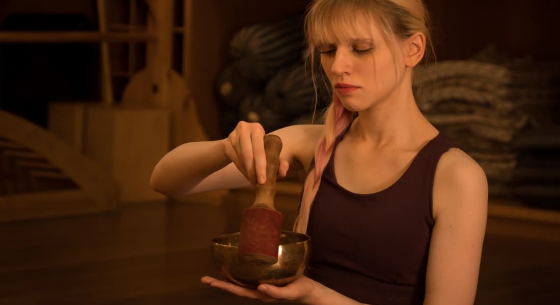 A blonde woman in a tank top with a Tibetan bowl