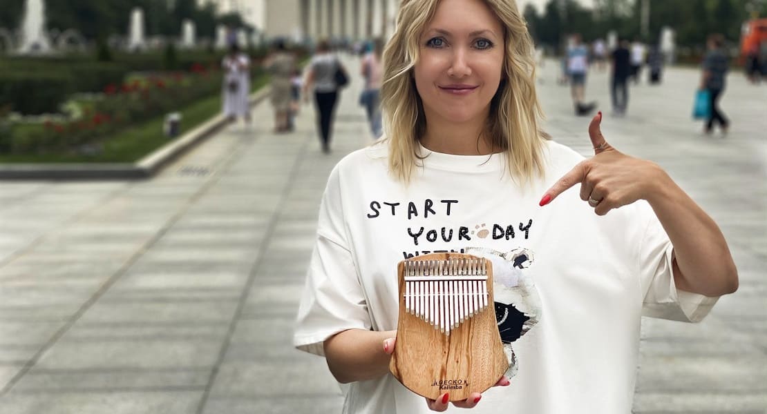 A blonde woman in a T-shirt holding a kalimba
