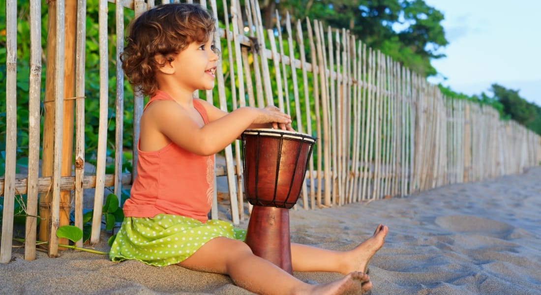 A child sitting on the beach with a djembe