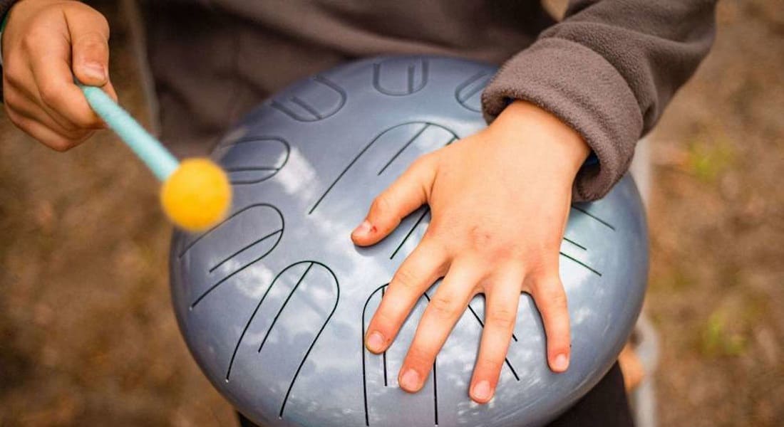 Close-up of a tongue drum with a hand holding a mallet