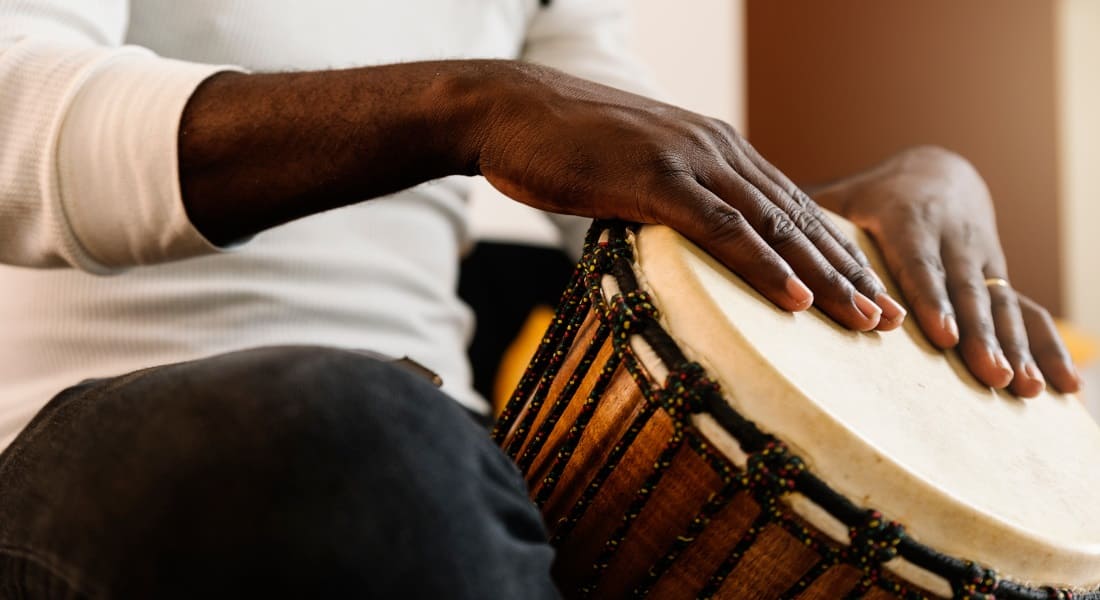 A close-up of a Black man playing a djembe