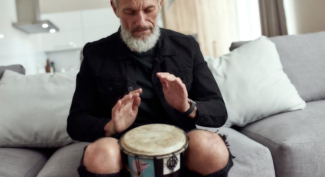 An elderly person playing a djembe