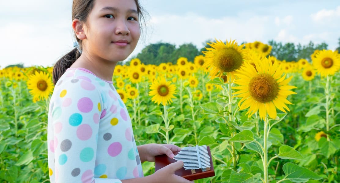 A girl holding a kalimba in a sunflower field
