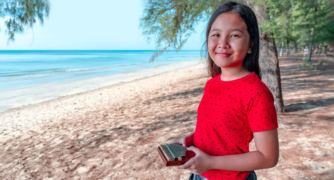 A girl holding a thumb piano on the beach