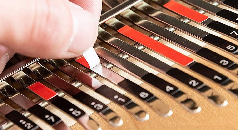 A hand placing stickers on a kalimba