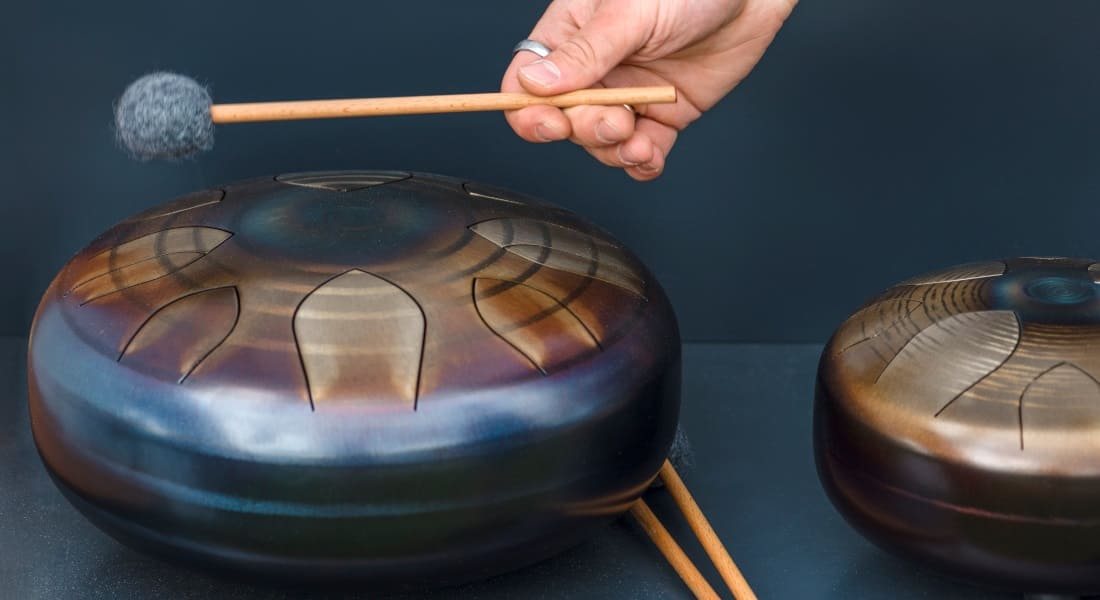 A hand holding a mallet next to a tongue drum