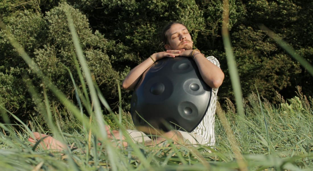 A handpan player sitting in the grass