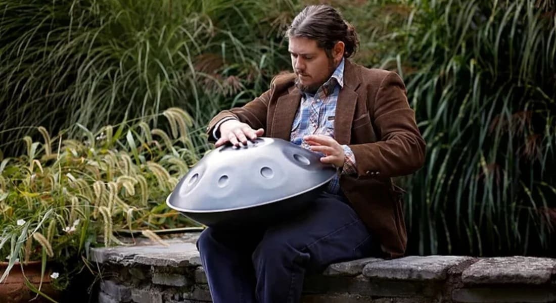 Jacob Cole playing the handpan on a low wall