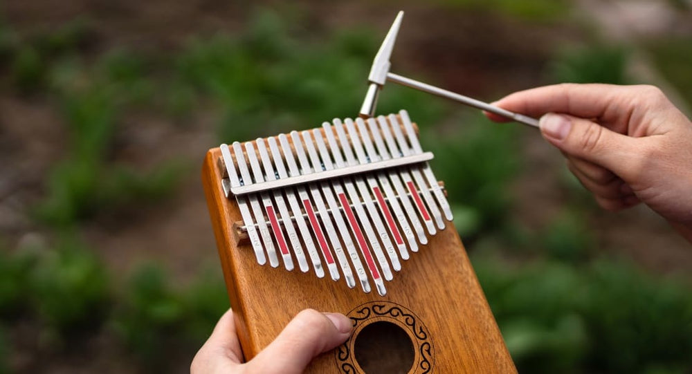 A kalimba held in the hand with a tuning hammer