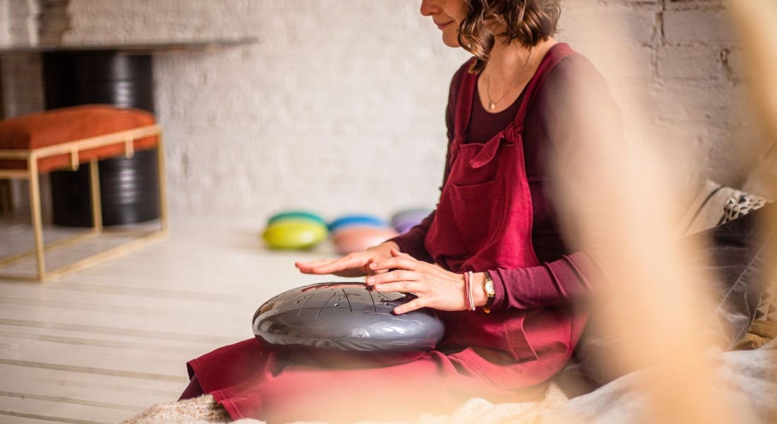 A kneeling woman playing a hank drum