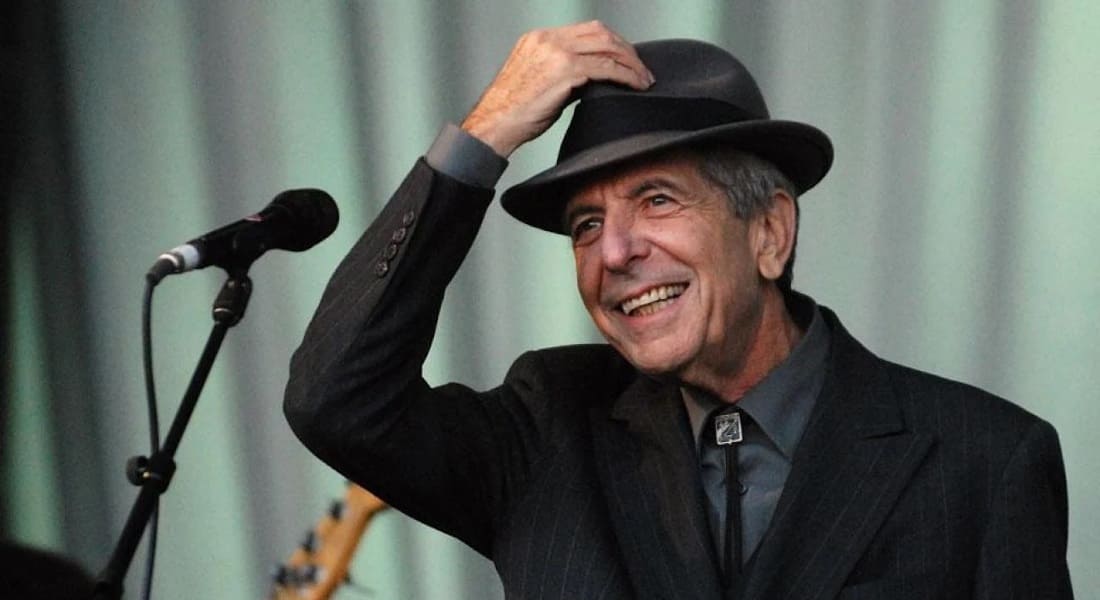 Leonard Cohen wearing a hat seated in front of a microphone