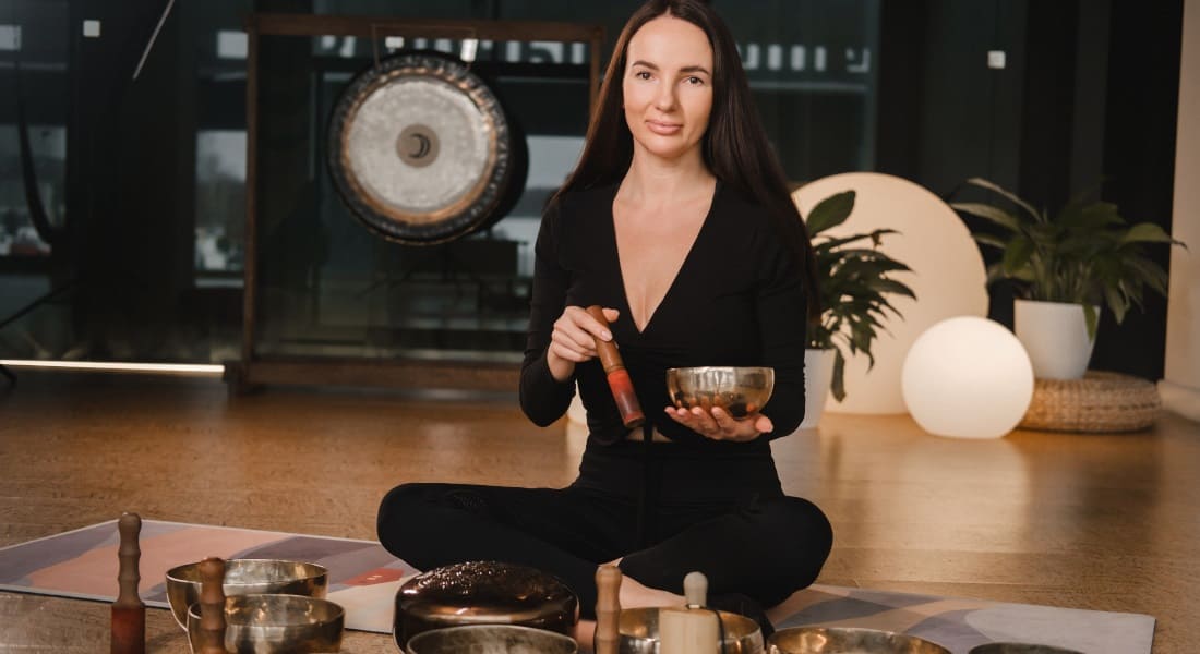 A woman in lotus pose surrounded by Tibetan singing bowls
