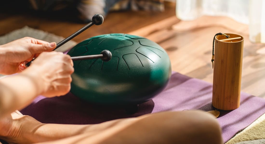 A man sitting cross-legged playing a green tongue drum