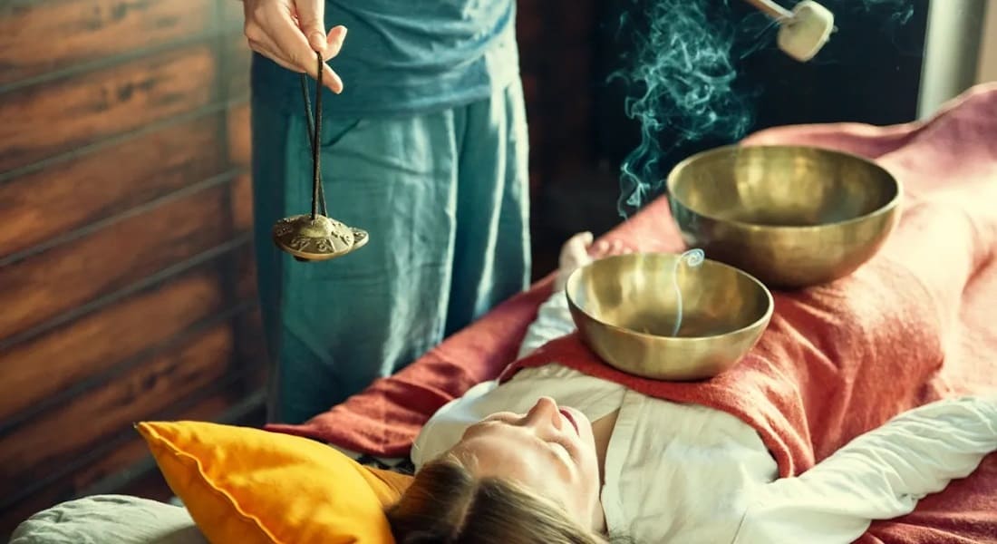 A man giving a sound massage to a woman with 7-metal Tibetan singing bowls