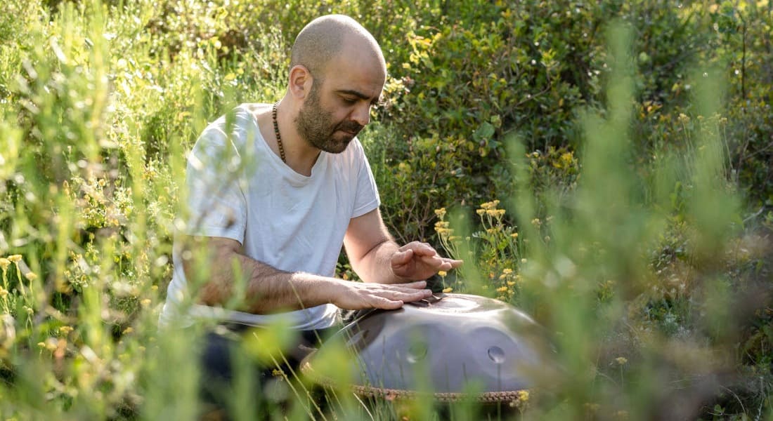 A man in a forest playing a travel handpan