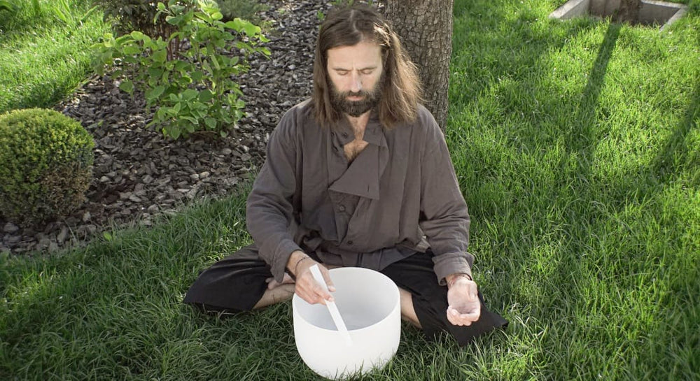 A man sitting on the floor playing a crystal singing bowl
