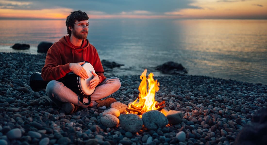Man sitting near a fire with a djembe