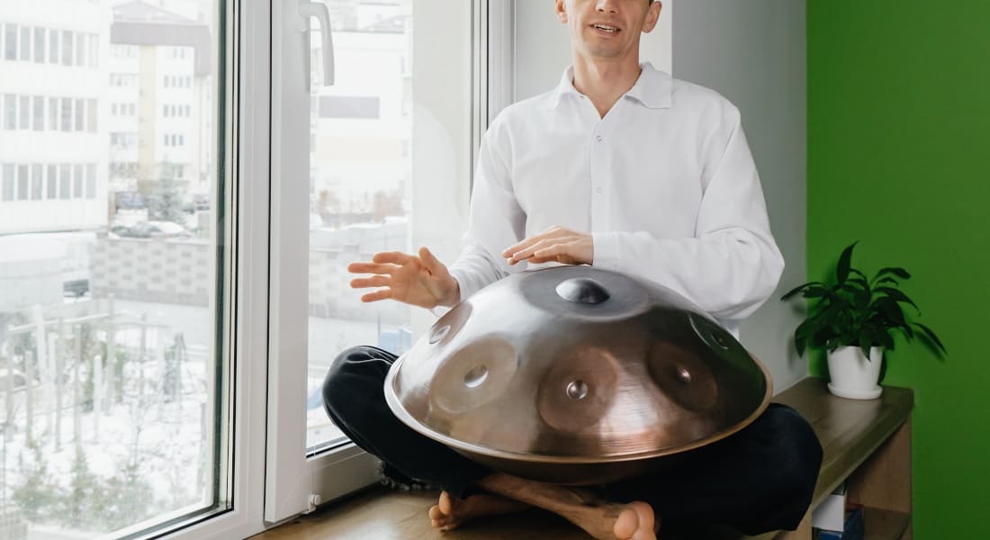 A man sitting on a piece of furniture playing a Hang