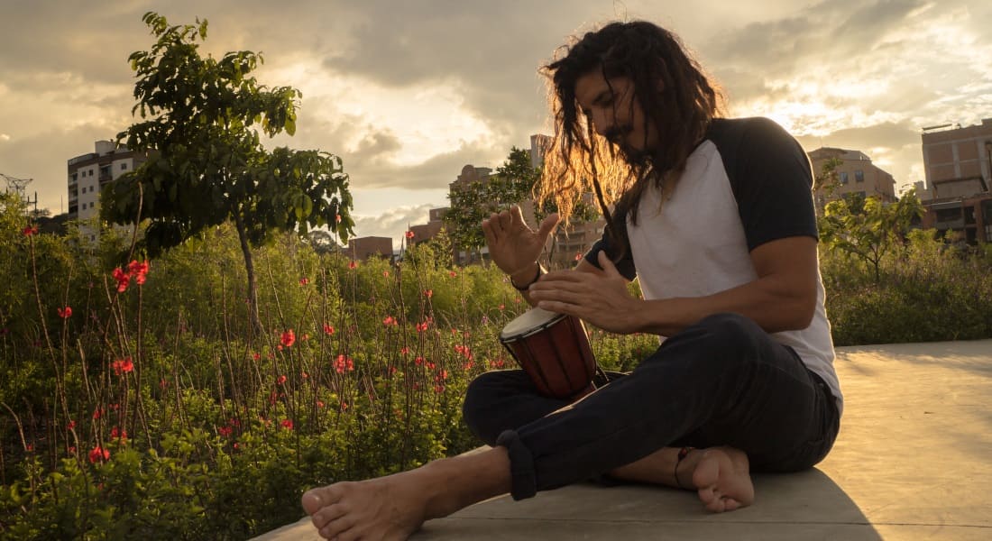 A seated man playing a tiny djembe