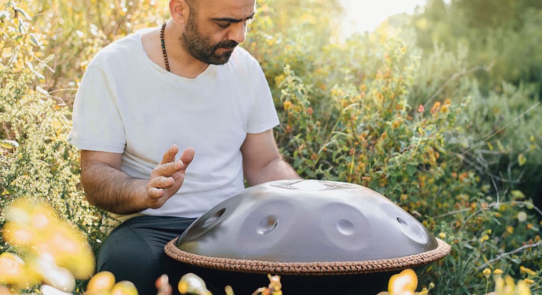A man striking a handpan in nature