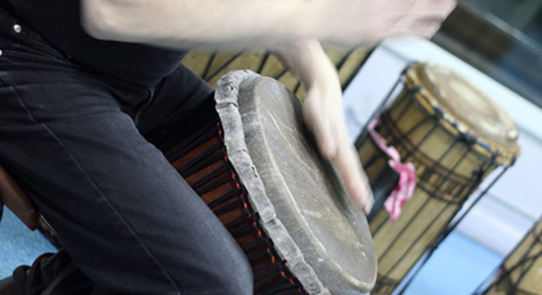 A person playing a djembe while seated