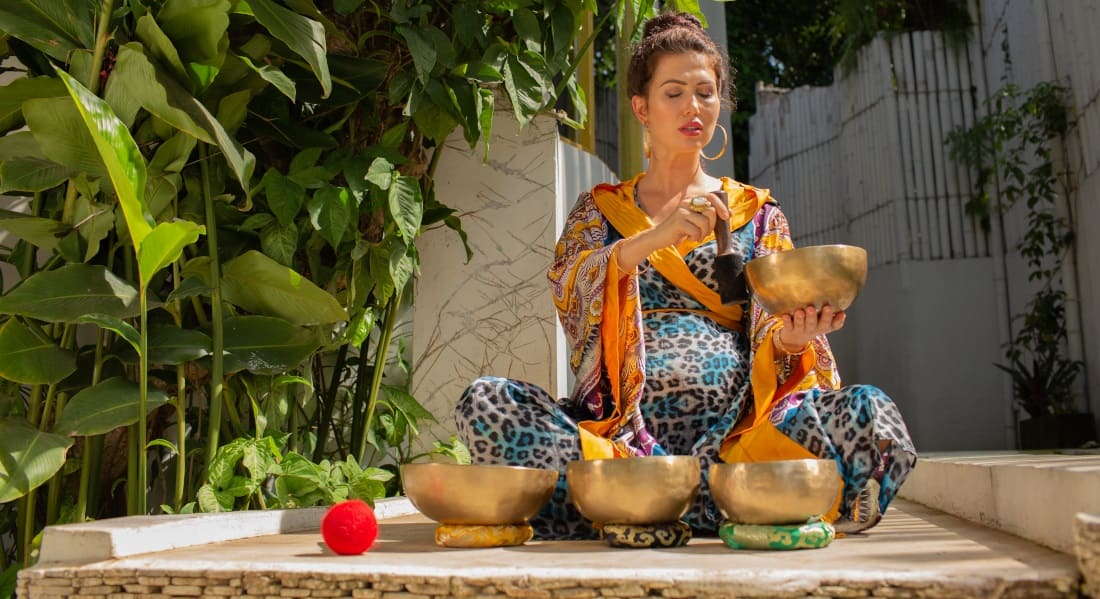 A pregnant woman sitting cross-legged with Tibetan singing bowls