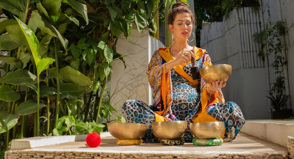 A pregnant woman sitting on the floor playing a Tibetan singing bowl