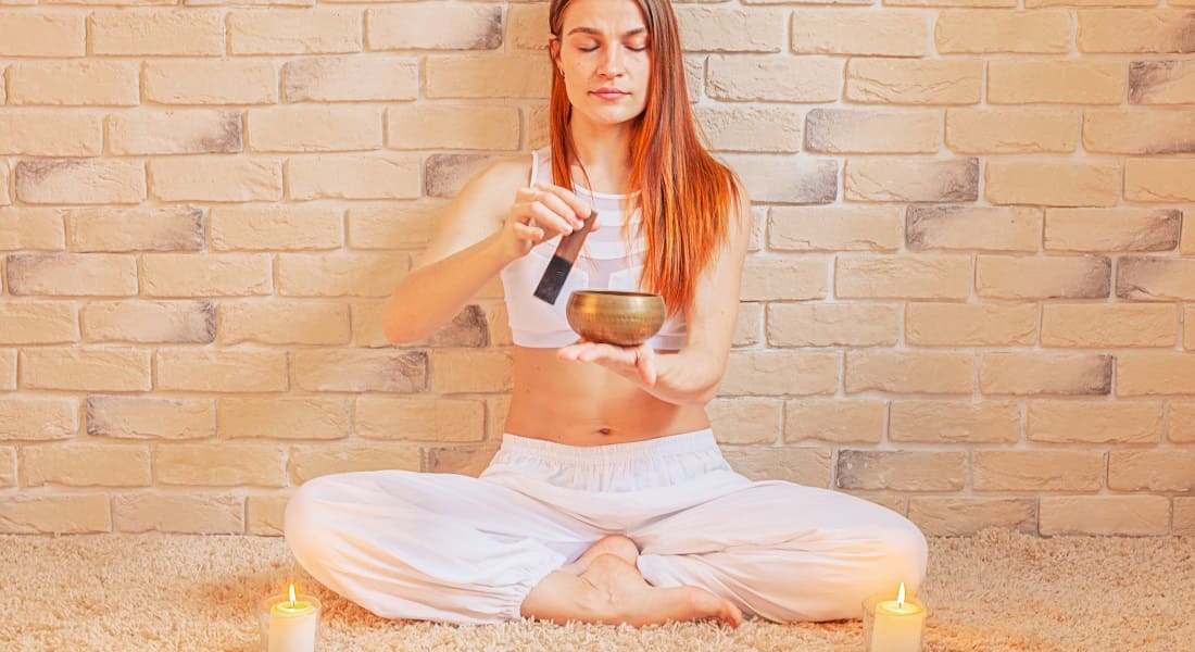 A red-haired woman holding a Tibetan bowl with two candles next to her
