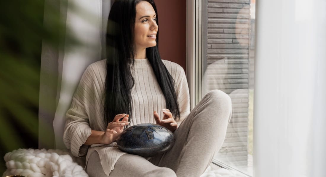 A seated brunette woman playing a steel tongue drum