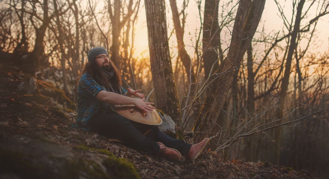 A percussionist seated in the forest with a handpan