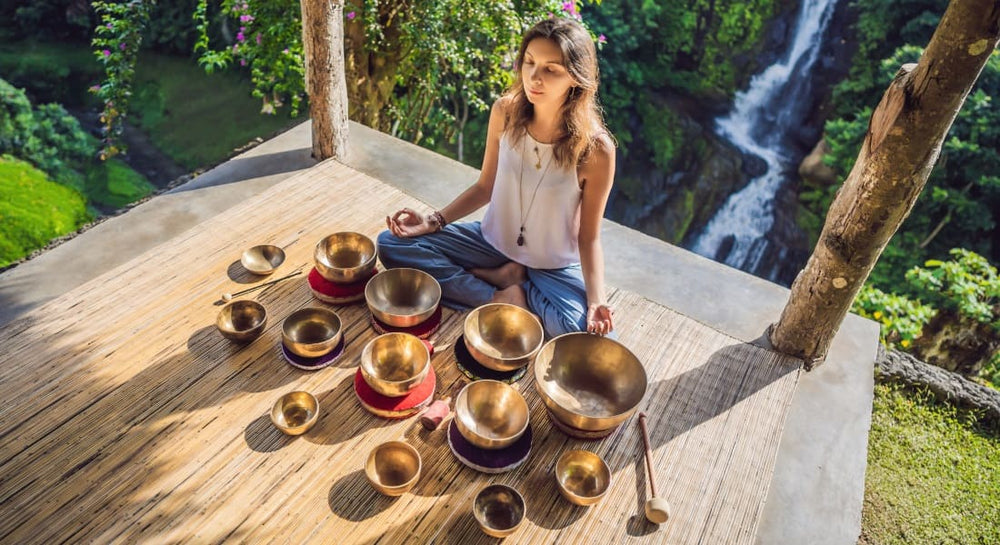 A seated woman meditating with about twenty Tibetan singing bowls