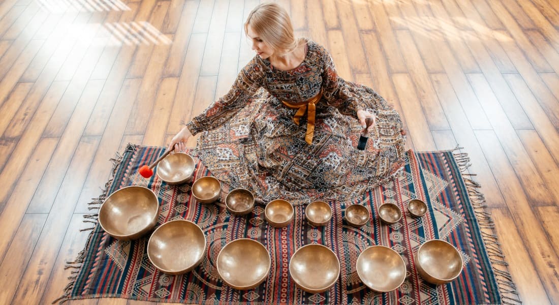 Several Tibetan singing bowls on a rug while a woman plays them